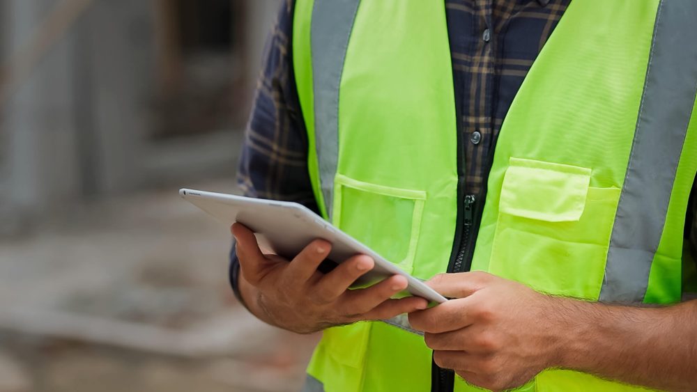 A person in a green construction vest using a tablet