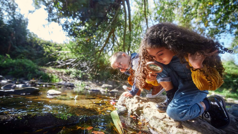Two kids examining a pond with magnifying glasses