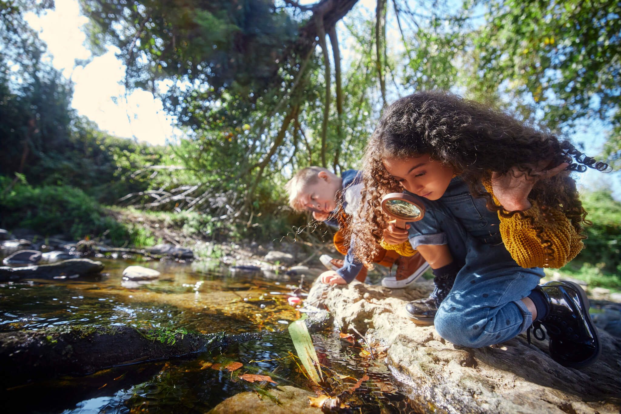 Two kids examining a pond with magnifying glasses