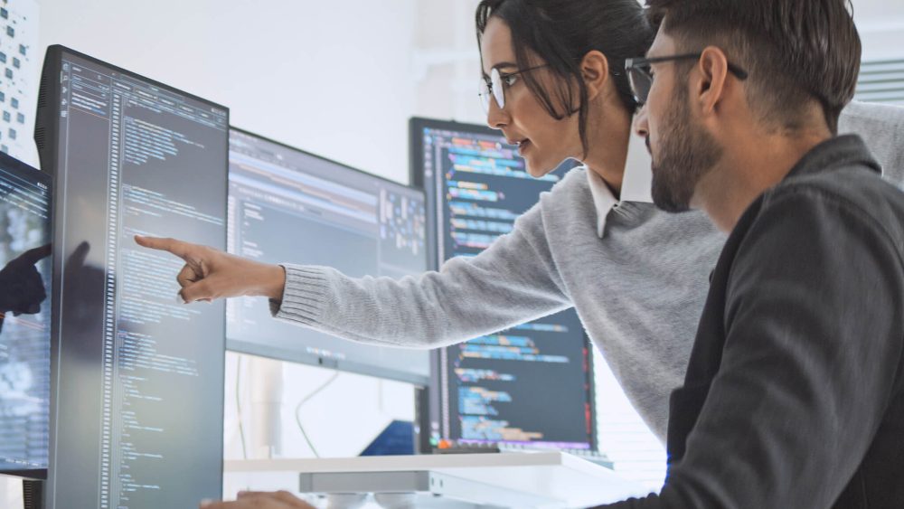 Two people looking at data on an array of monitors