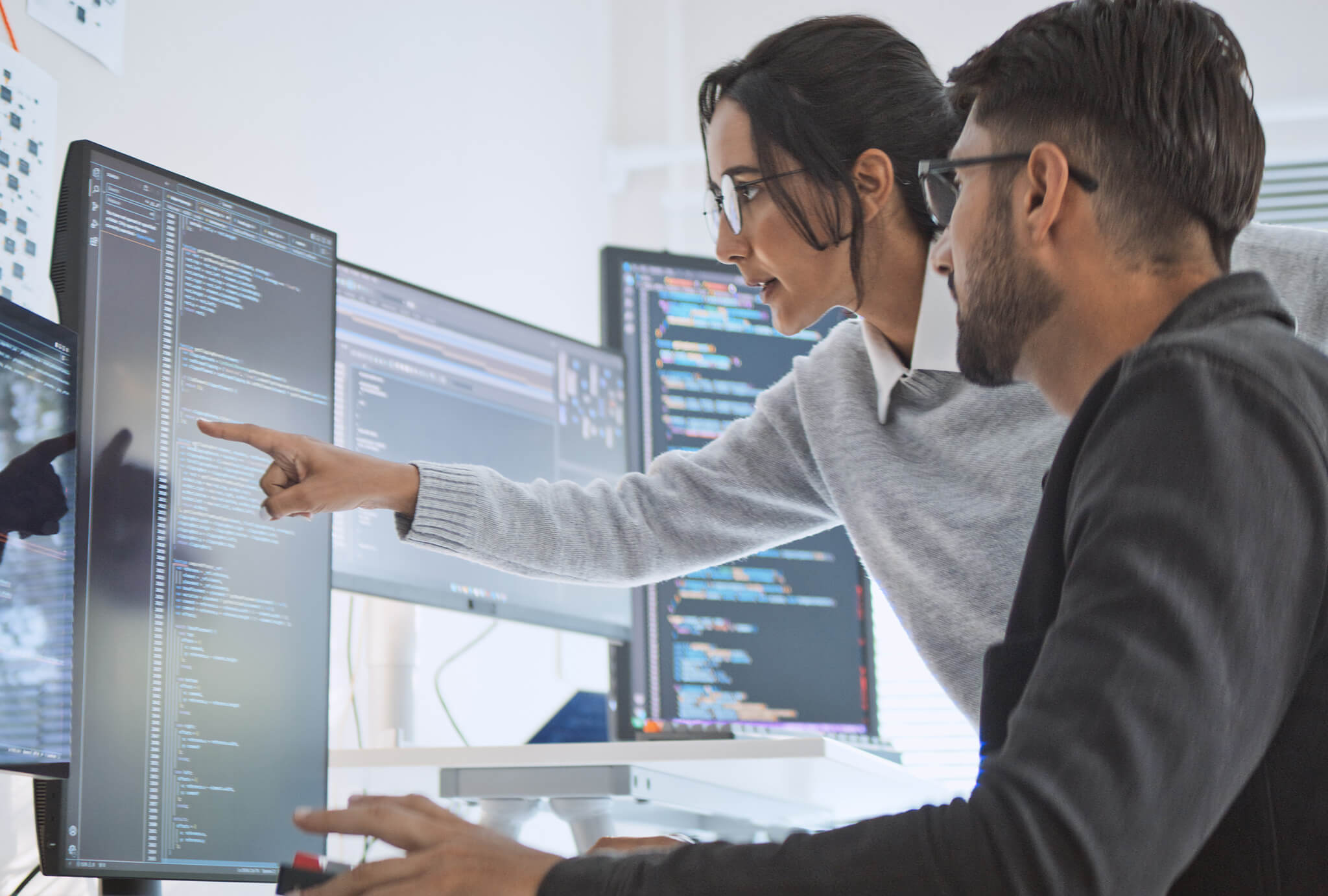 Two people looking at data on an array of monitors