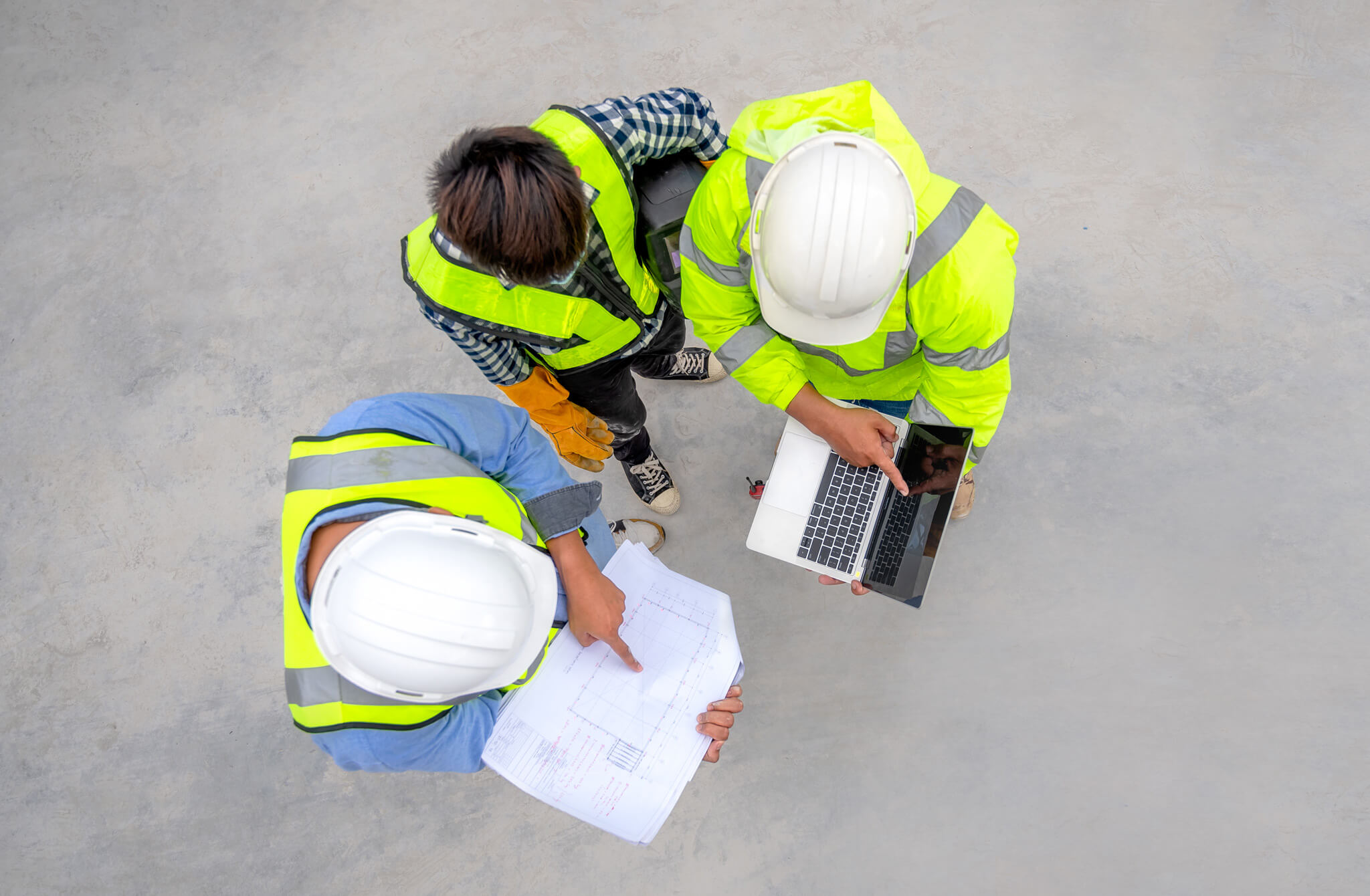 Three workers inspect a blueprint and laptop